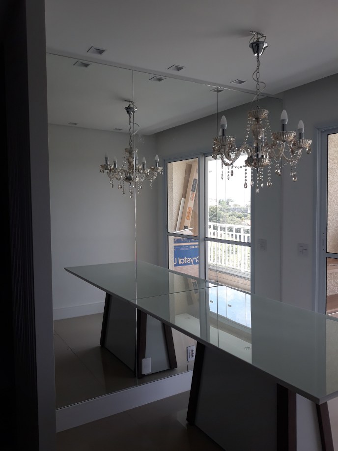 Sala de jantar com espelho na parede, mesa com tampo de vidro e lustre de cristal