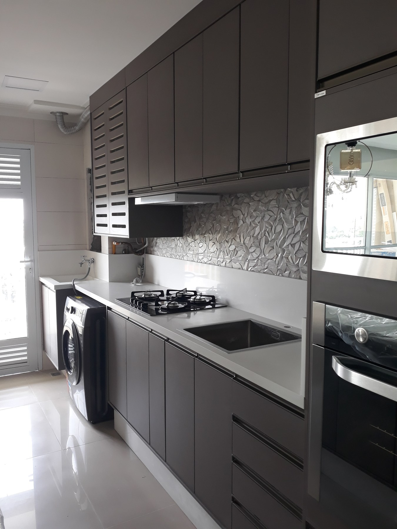Cozinha planejada com cooktop, cuba embutida, revestimento em relevo e área de serviço integrada