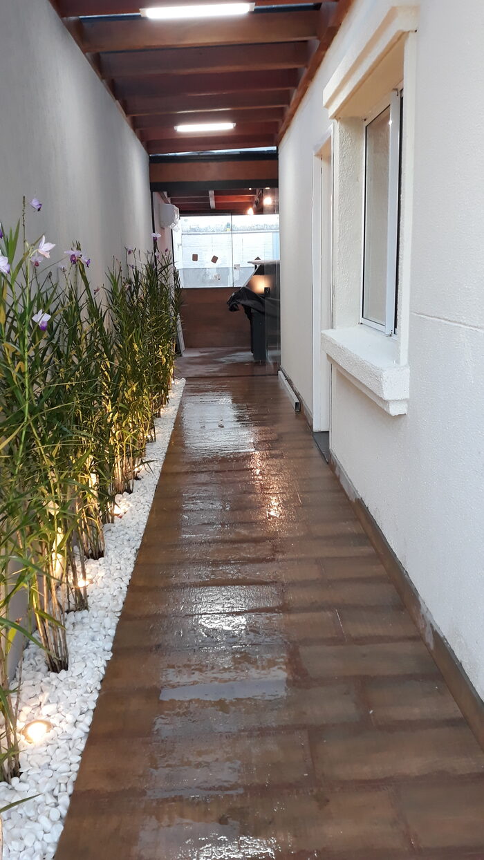 Corredor externo jardinado com deck de madeira e iluminação embutida